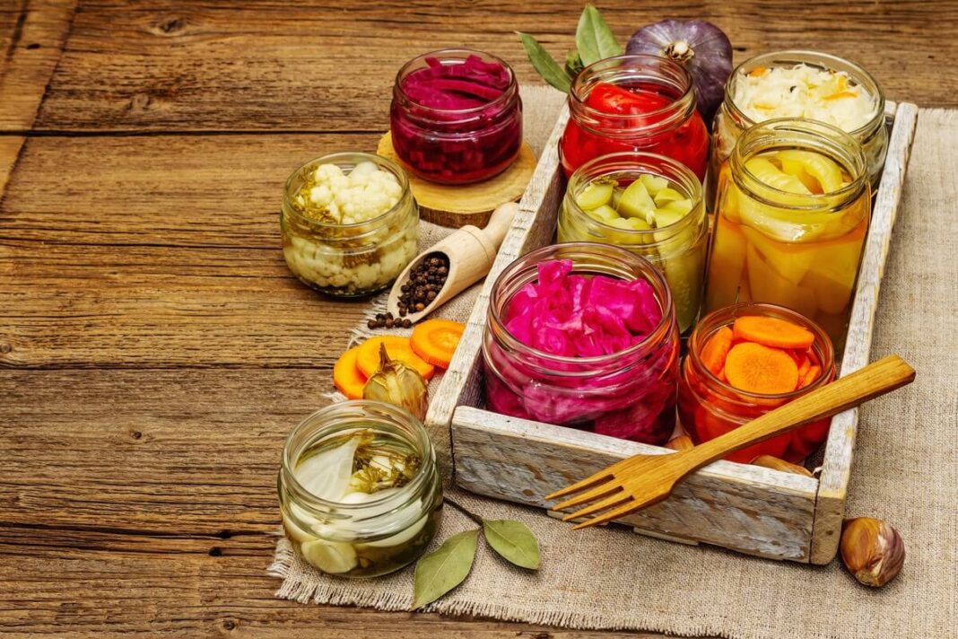 Sveiko žarnyno maistas – įvairių spalvų fermentuotų daržovių stiklainiai ant medinio stalo.