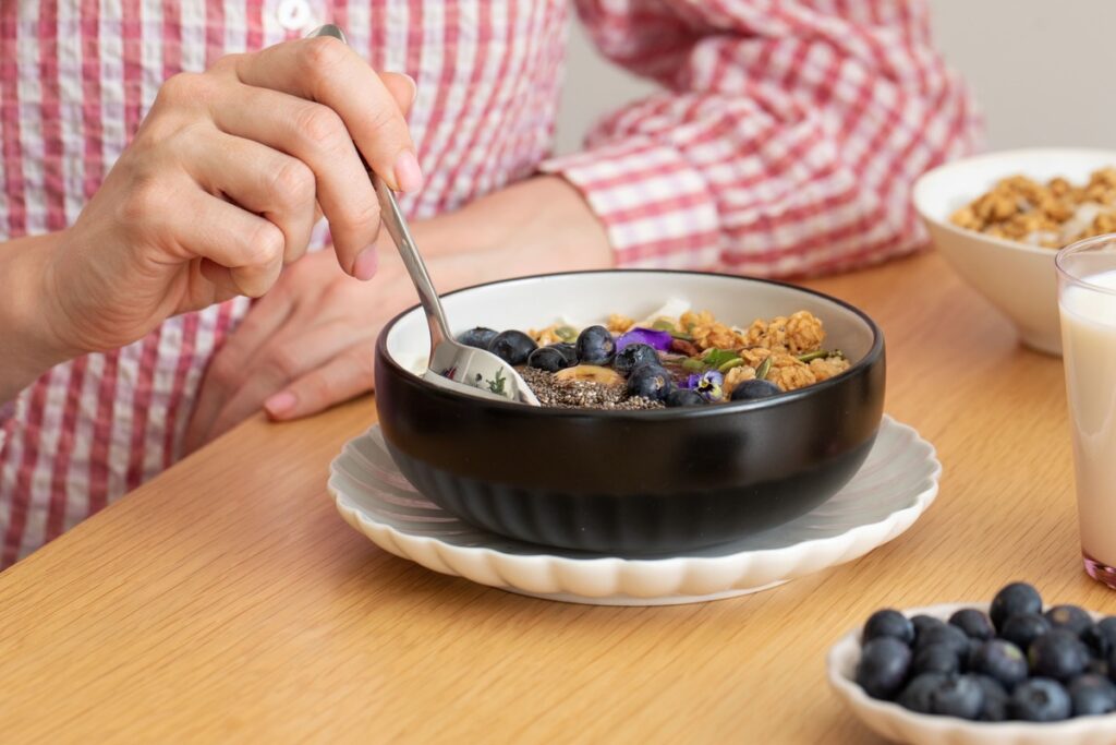 uogos nuo vėžio – dubenėlis su mėlynėmis, granola ir chia sėklomis ant medinio stalo.