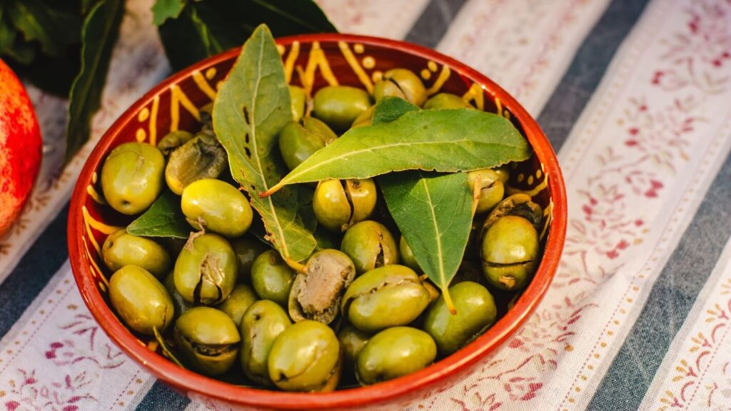 alyvmedžio lapų nauda atskleista dubenyje su žaliosiomis alyvuogėmis ir šakelėmis ant staltiesės