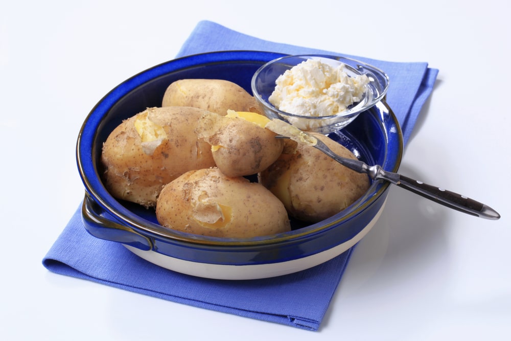 Bulvių virimas su lupenomis, patiektos virtos bulvės su varške mėlyname inde.