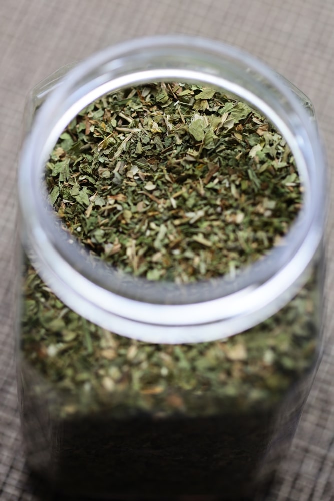 Džiovintos žolelės stiklinio indelio viduje, fotografuotos iš viršaus.