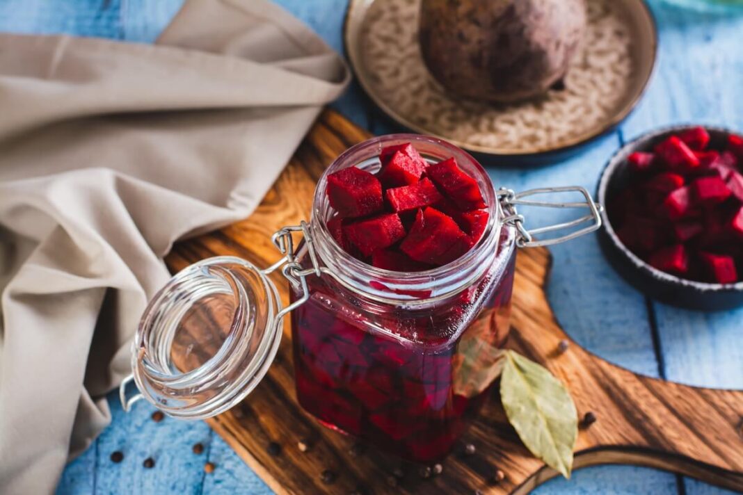 marinuoti burokėliai stiklainyje su ryškiais kubeliais ir prieskoniais ant medinės lentos