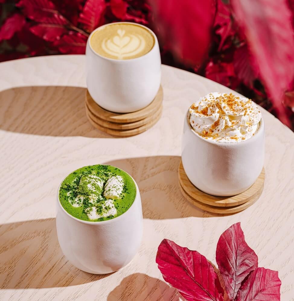 matcha sveikesnė kava baltuose puodeliuose su pieno puta ir natūralia žalia spalva ant medinio stalo