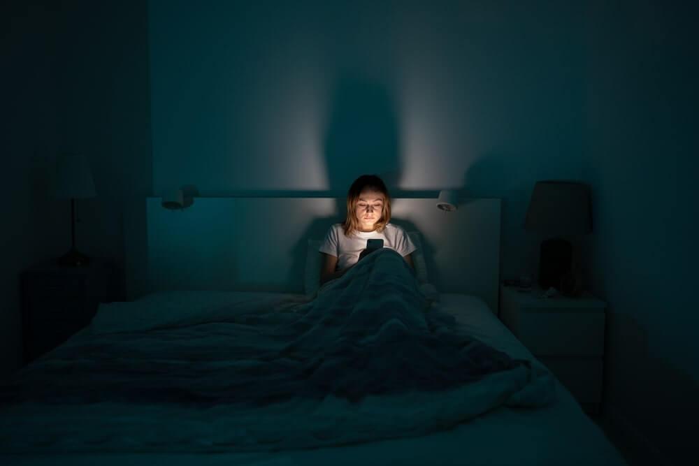 naktinė šviesa ir širdies sveikata vaizduojama moteriai skaitant telefoną tamsioje patalpoje