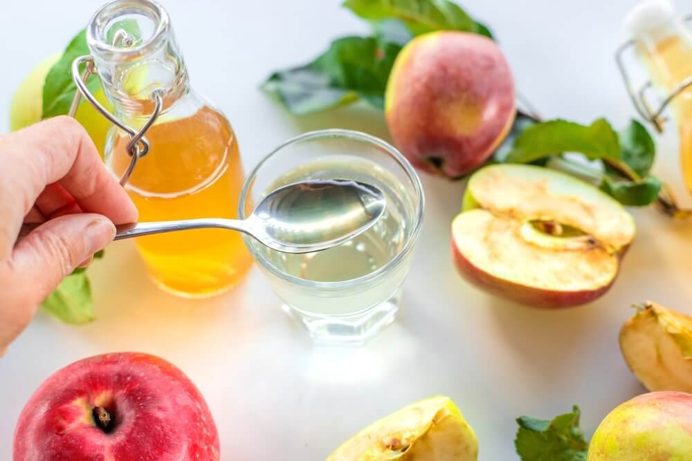 Obuolių sidro actas maišomas su vandeniu stiklinėje šalia obuolių ir lapų
