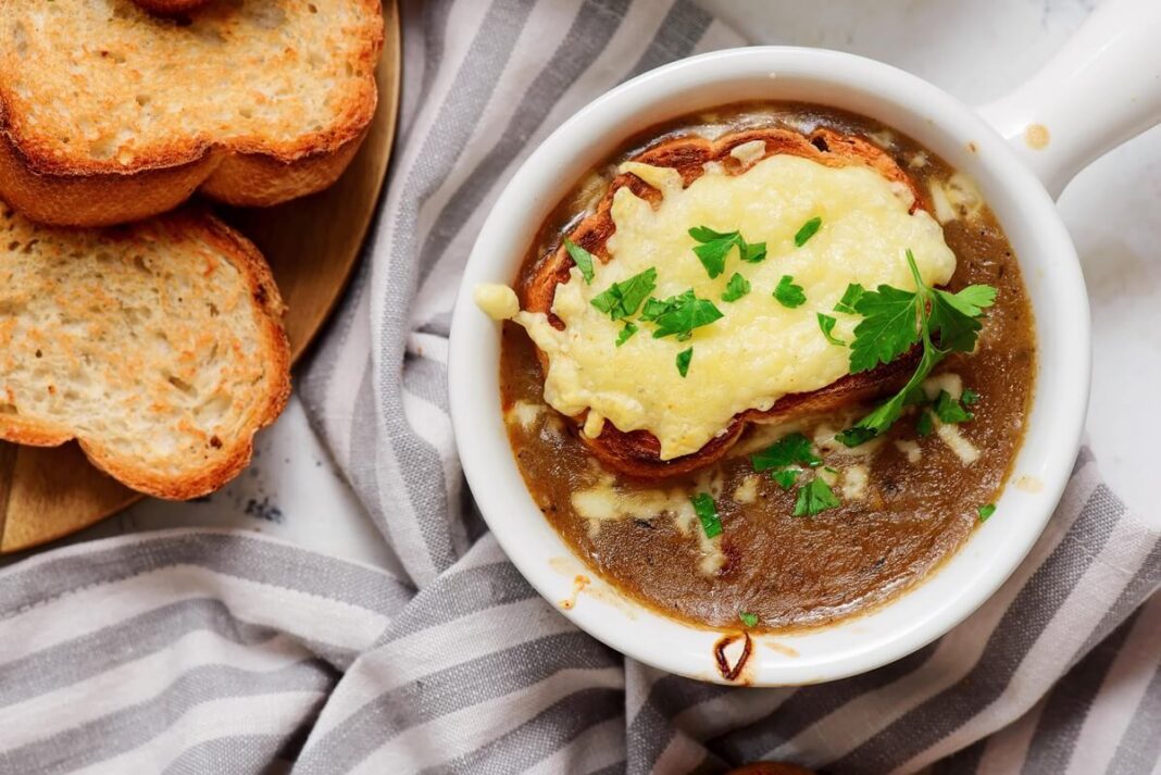 Prancūziška svogūnų sriuba su apkepinta bagete ir tirpstančiu gruyere sūriu, papuošta žalumynais