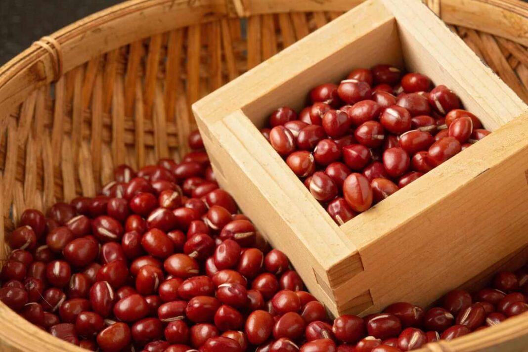 Adzuki pupelės supiltos į tradicinį kvadratinį medinį indelį, esantį pintame krepšyje.