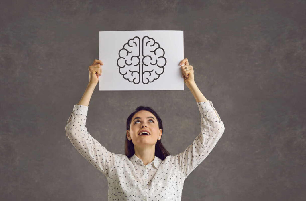 Atminties gerinimas iliustruojamas moterimi, kuri virš galvos laiko popieriaus lapą su smegenų grafiniu vaizdu.