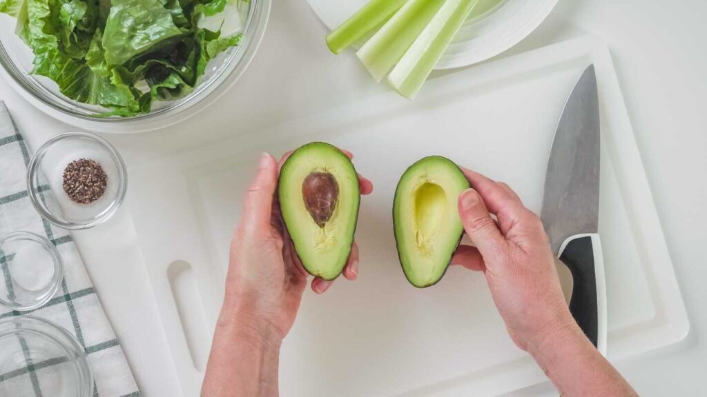 avokadas po 60, perpjautas avokadas laikomas rankose šviesioje virtuvėje