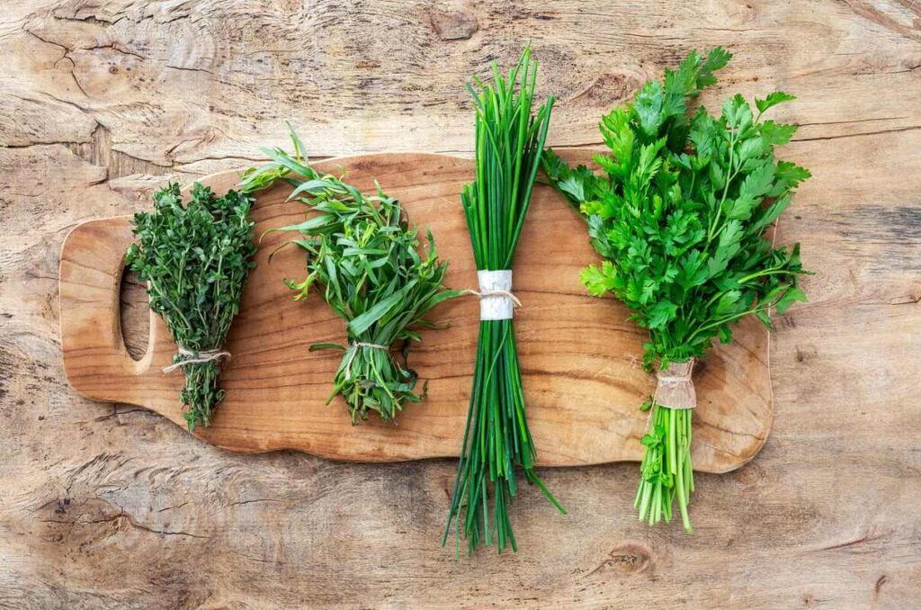 Daržovės žiemą – petražolių, laiškinių česnakų ir čiobrelių ryšulėliai ant medinės lentos.