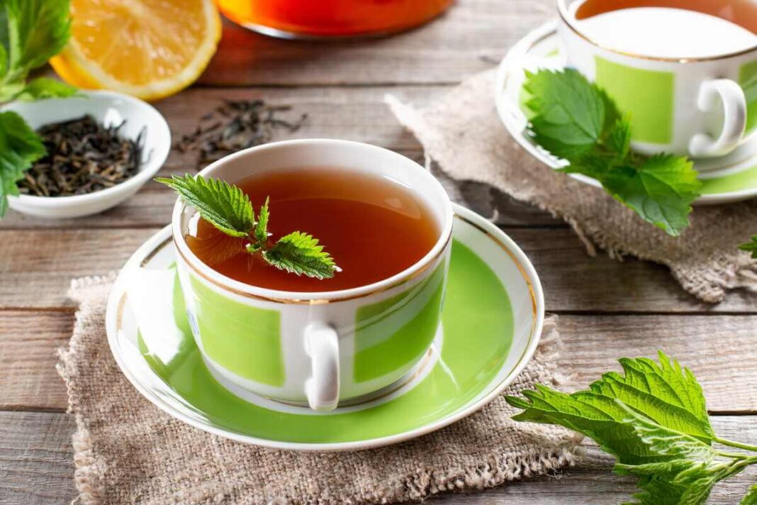 dilgėlių arbata ir cukraus kiekis žalios spalvos puodelyje ant medinio stalo