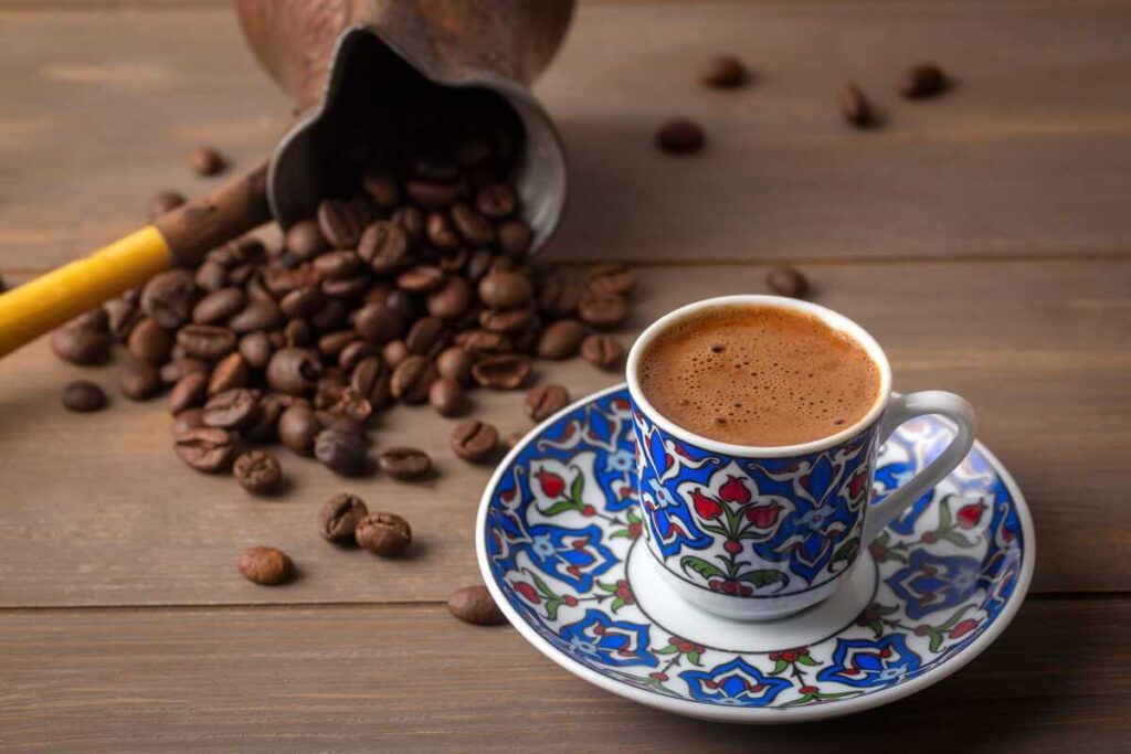 kava tuščiu skrandžiu patiekiama puodelyje šalia pabirusių kavos pupelių ant medinio stalo