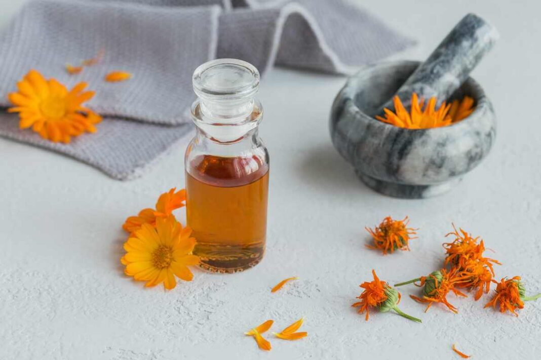 medetkų aliejus, stiklinis buteliukas su aliejumi ir šviežiais medetkų žiedais šviesiame fone