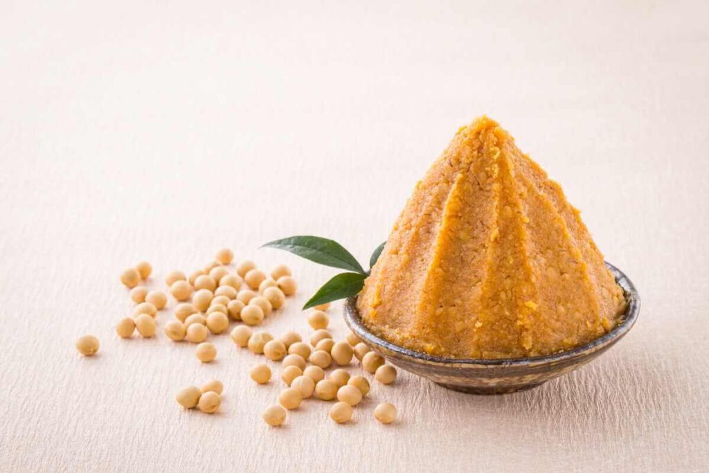 miso nauda sveikatai fermentuota miso pasta dubenėlyje su sojų pupelėmis ant šviesaus fono