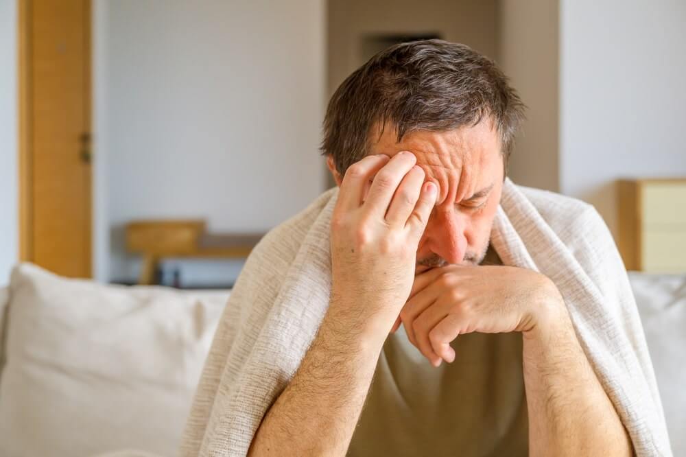 pagirios po švenčių vyras sėdi ant sofos laikydamas galvą dėl stipraus galvos skausmo