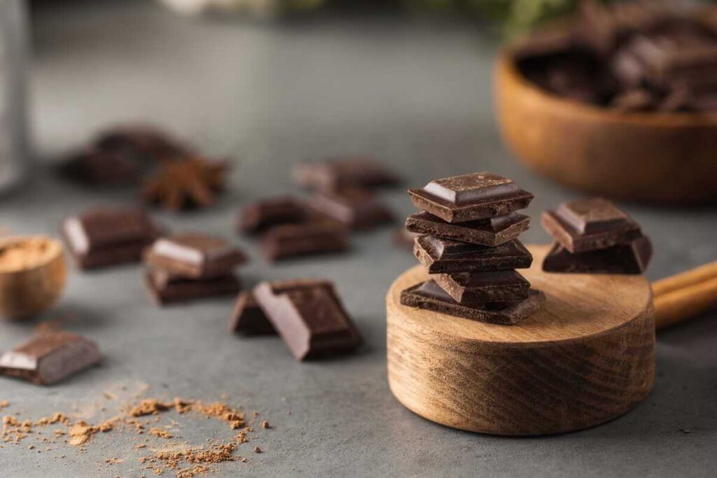 šokoladas ir kava vaizduojami per juodojo šokolado gabalėlius ant medinio paviršiaus