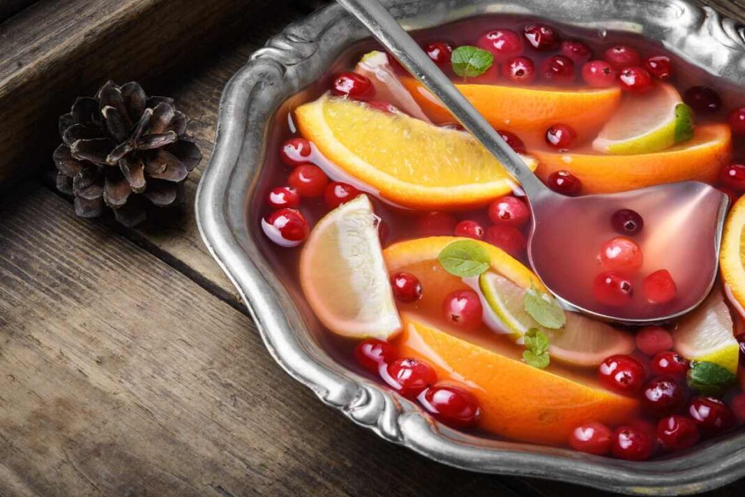 spanguolių punšas metaliniame inde su apelsinų skiltelėmis, spanguolėmis ir prieskoniais