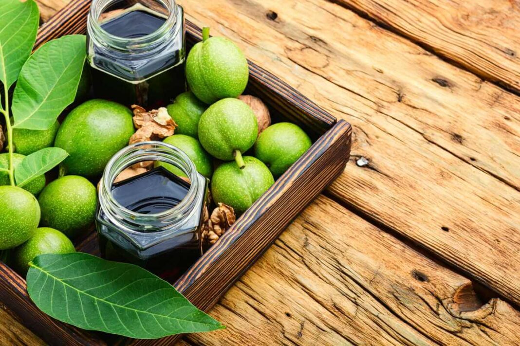 vaistas iš žalių graikinių riešutų, stiklainiai su tamsiu užpilu ir šviežiais žaliais riešutais