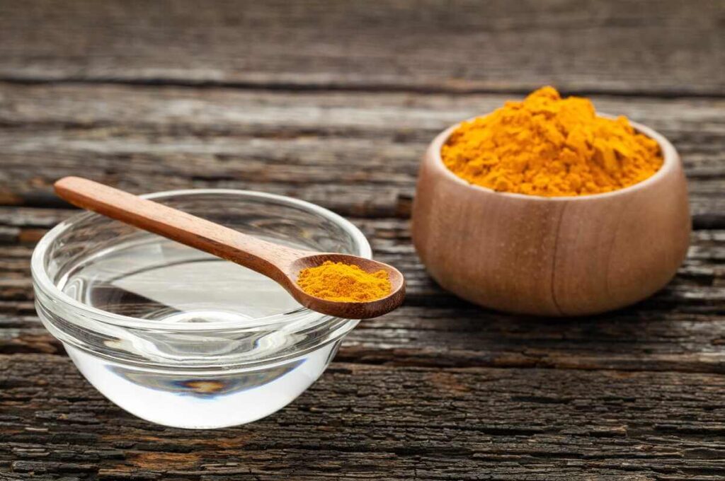 vanduo su ciberžole ryte, stiklinė šilto vandens su ciberžole ant medinio stalo