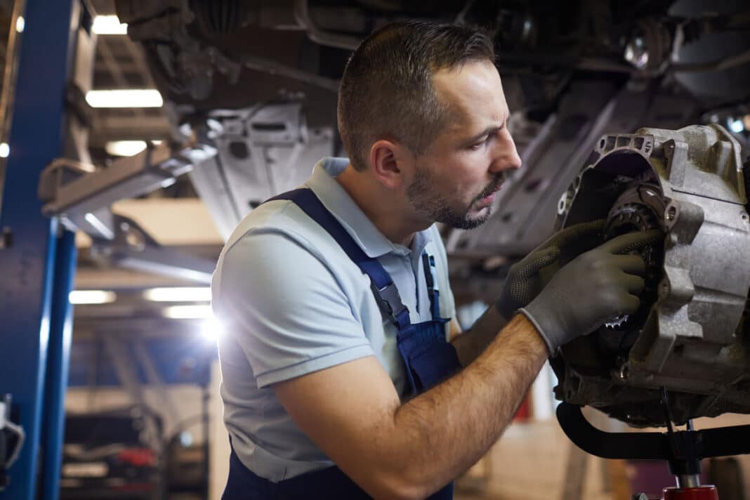 Variklio ir greičių dėžės apsaugos visureigiams – autoserviso specialistas tikrina transmisijos mazgus ir dugno apsaugos būklę pakeltame automobilyje.