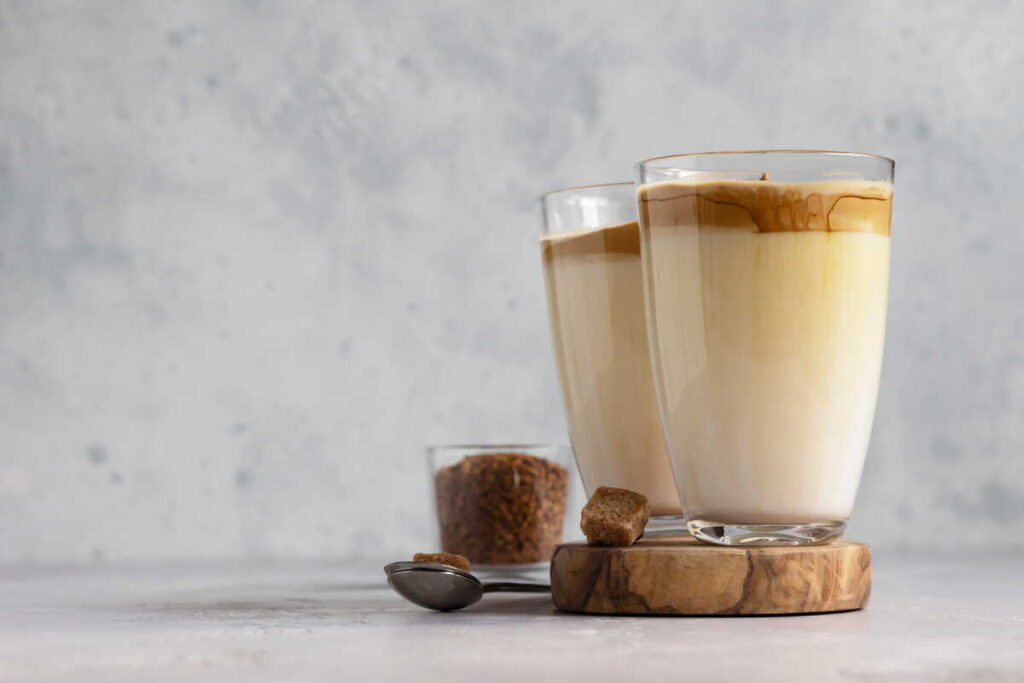 Ar kavos su pienu gėrimas padeda kovoti su uždegimu demonstruojant du sluoksniuotus gėrimus aukštose stiklinėse.