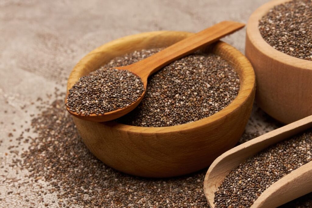 chia sėklos svoriui suberti į natūralaus medžio dubenėlį su mediniu šaukštu ant akmeninio paviršiaus.