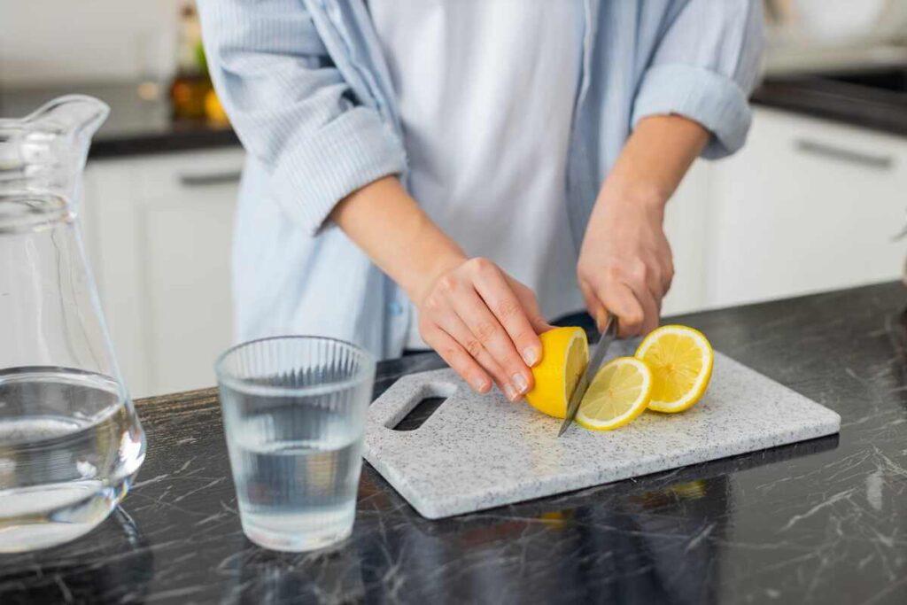 Citrinų laikymas prasideda nuo vaisiaus pjaustymo lygiais griežinėliais ant pilkos lentelės šviesioje virtuvėje