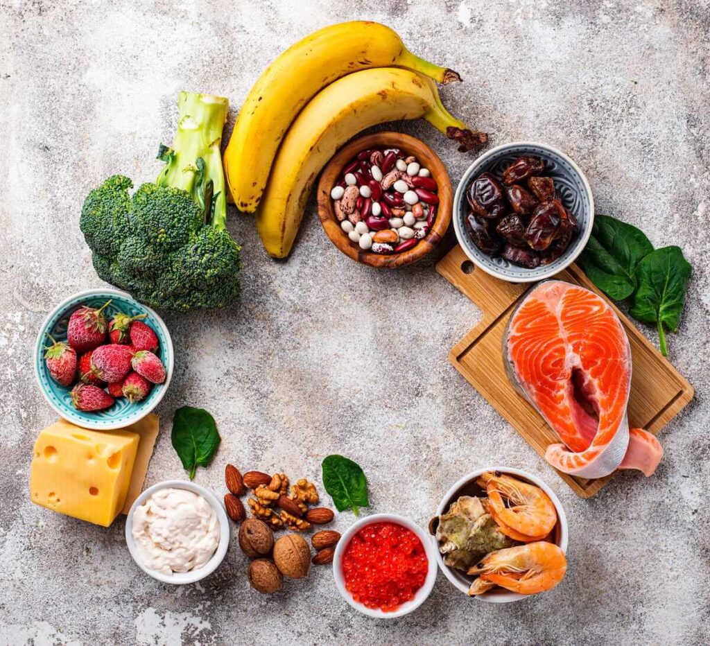 Dopamino kiekio didinimas per mitybą iliustruojamas spalvingais vaisiais, žuvimi ir riešutais.