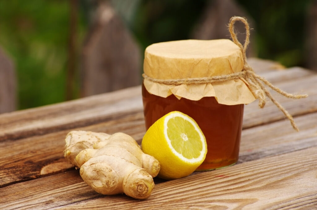 Imbieras su citrina ir medumi padėtas ant medinio paviršiaus šalia stiklainio su geltonu mišiniu.