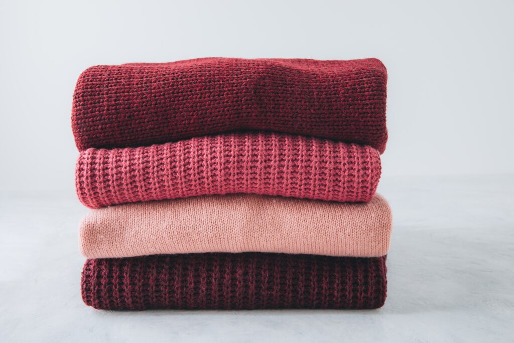 Šiltas megztinis žiemai tvarkingai sulankstytas į keturių skirtingų atspalvių sluoksnius ant lygaus paviršiaus.