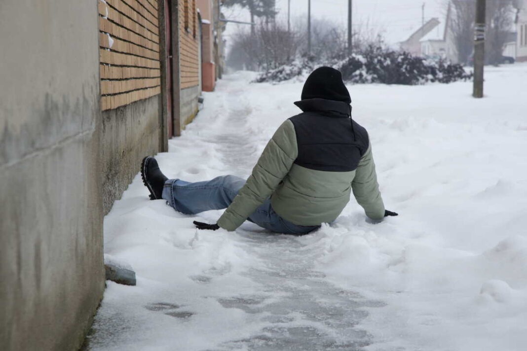 Slidus kiemas: ant apsnigto ir apledėjusio šaligatvio parkritęs žmogus žieminėje striukėje.