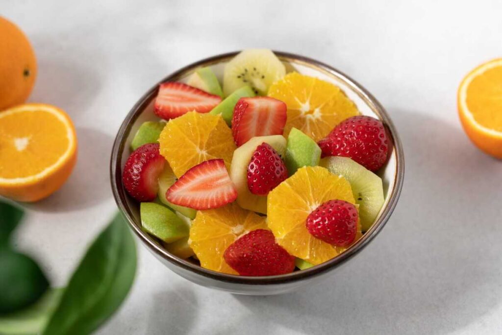 Vaisiai imunitetui stiprinti pateikiami dubenėlyje su pjaustytais apelsinais, braškėmis ir kiviais.