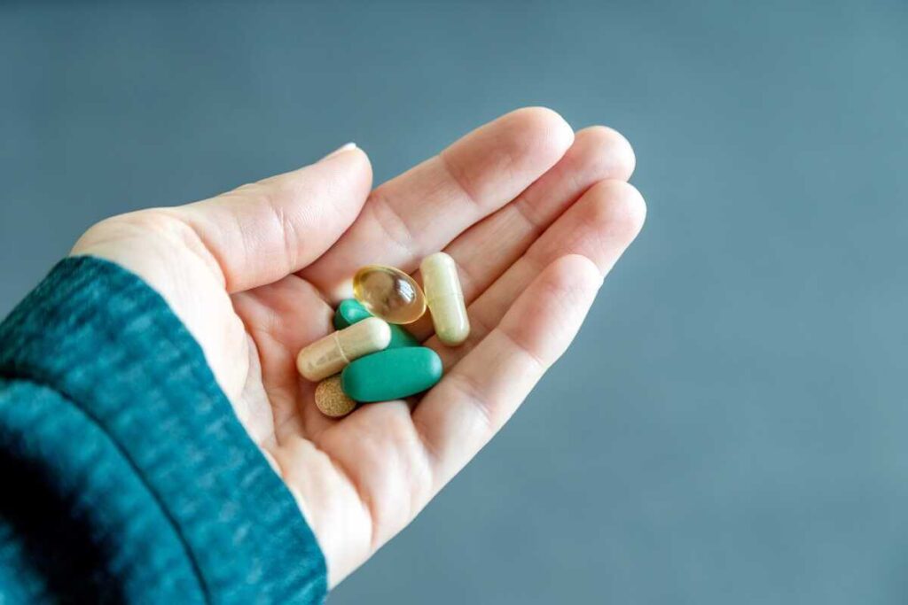 Vaistų vartojimas laikant spalvotas kapsules ir piliules atvirame delne pilkame fone.