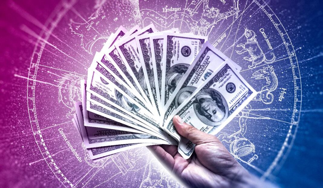 Ranka laiko išskleistus JAV dolerių banknotus zodiako ženklų fone