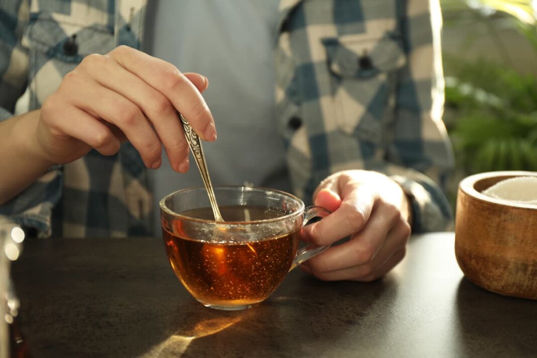 Žmogus maišo arbatą stikliniame puodelyje šalia keraminio puodelio