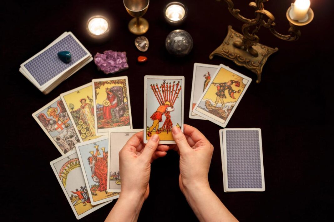 Tarot kortos, rankose laikoma Dešimties lazdų korta, žvakės ir krištolinis rutulys