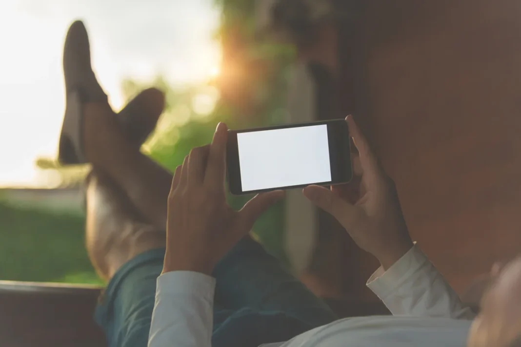Žmogus ilsisi laikydamas horizontalų išmanųjį telefoną prie lango